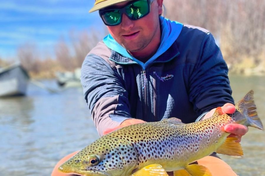 Man holding up a large brown trout while fly fishing on the riverbank in Montana.